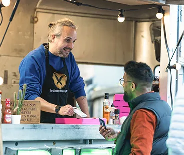 Market stall vendor handing a card reader to a customer for payment