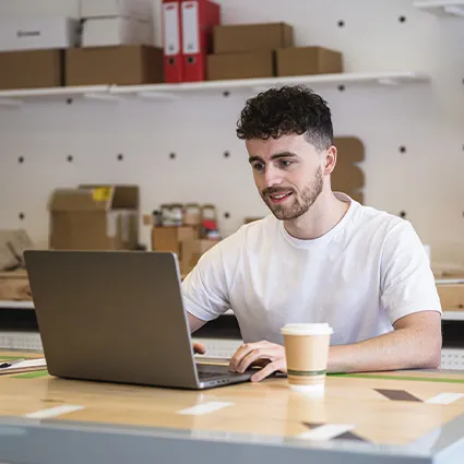 Person working at a desk using a laptop with a takeaway coffee nearby