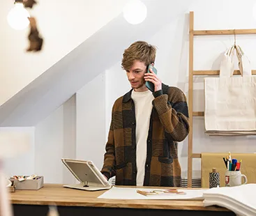 Small business owner standing behind a counter using a tablet and phone