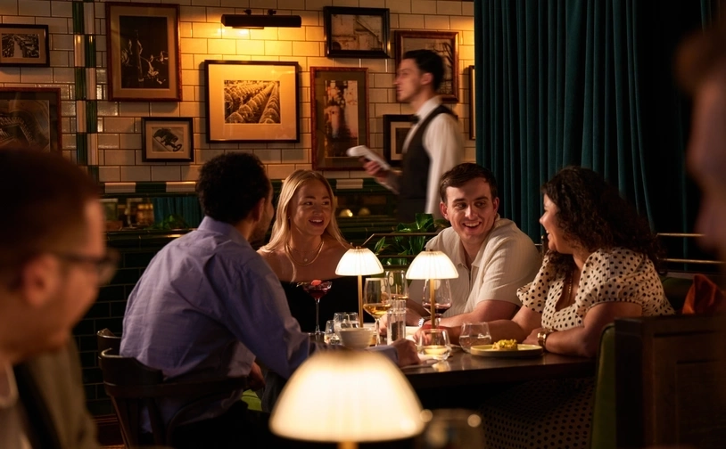 Group of customers dining together at a restaurant table with a server in the background