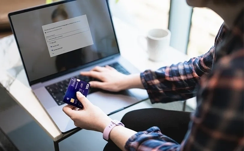 Person holding a payment card while completing an online payment on a laptop