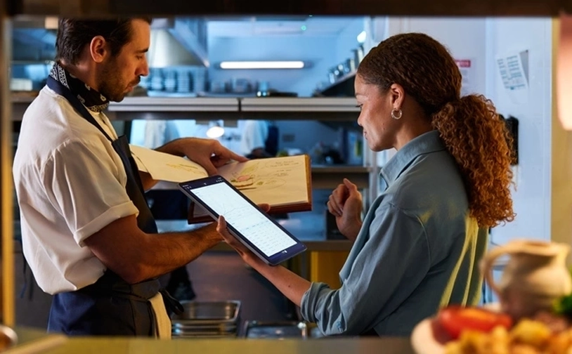 Restaurant staff using a tablet to manage orders and payments in a commercial kitchen