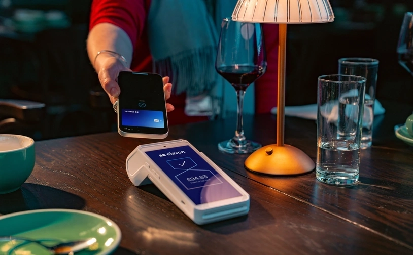Customer making a mobile contactless payment at a restaurant table using a card payment terminal