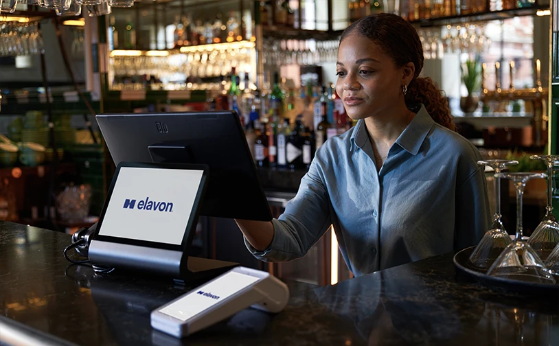 Restaurant staff member using an Elavon point of sale system behind a bar counter