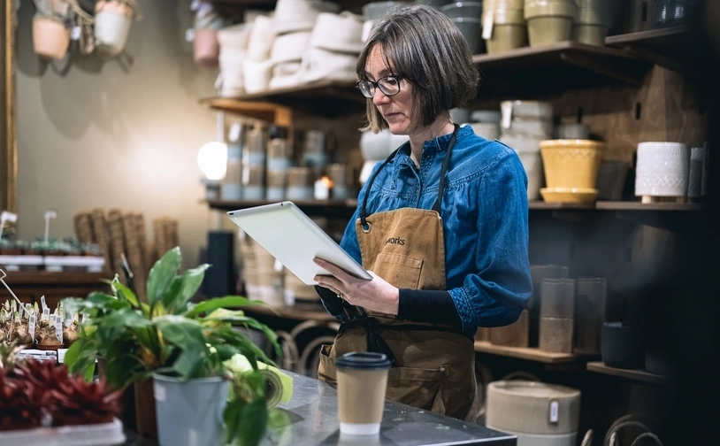 Shop worker using tablet at counter in plant and pottery store managing inventory and orders