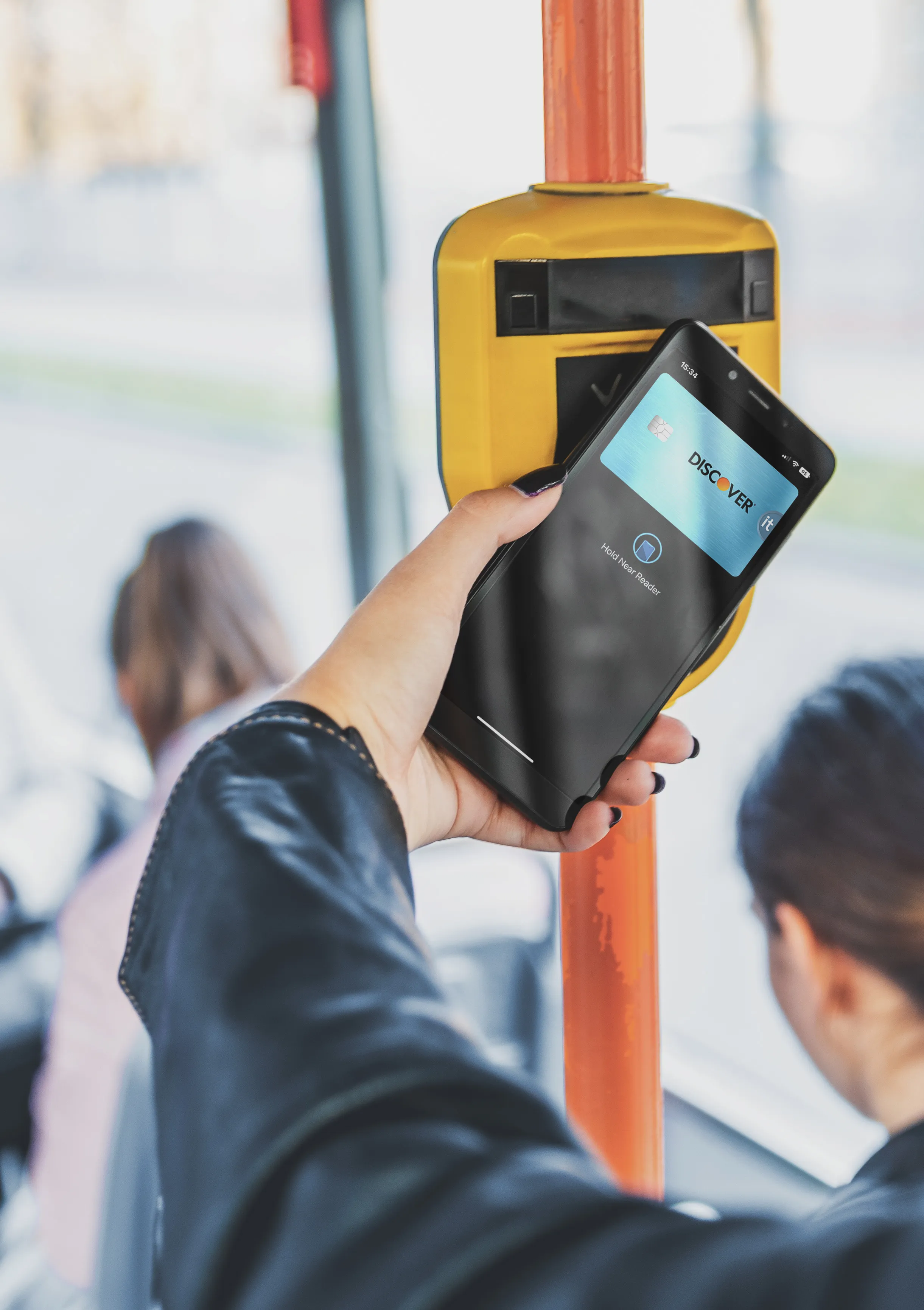 A person holds a smartphone against a contactless payment reader on public transport to tap in