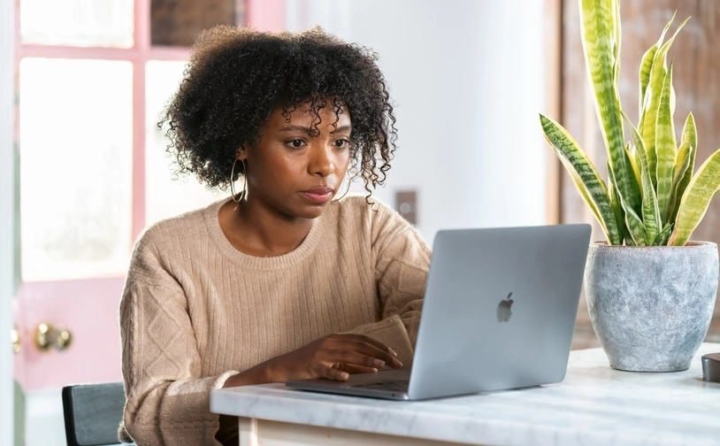 A happy woman sits tapping at a laptop