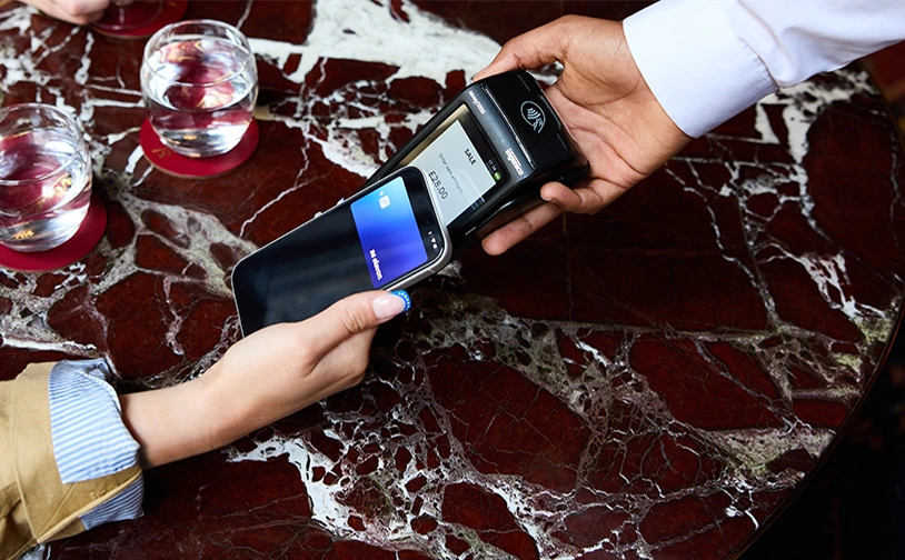 Customer making a contactless mobile payment using a smartphone and card reader on a restaurant table, demonstrating secure digital payment technology and modern point of sale solutions