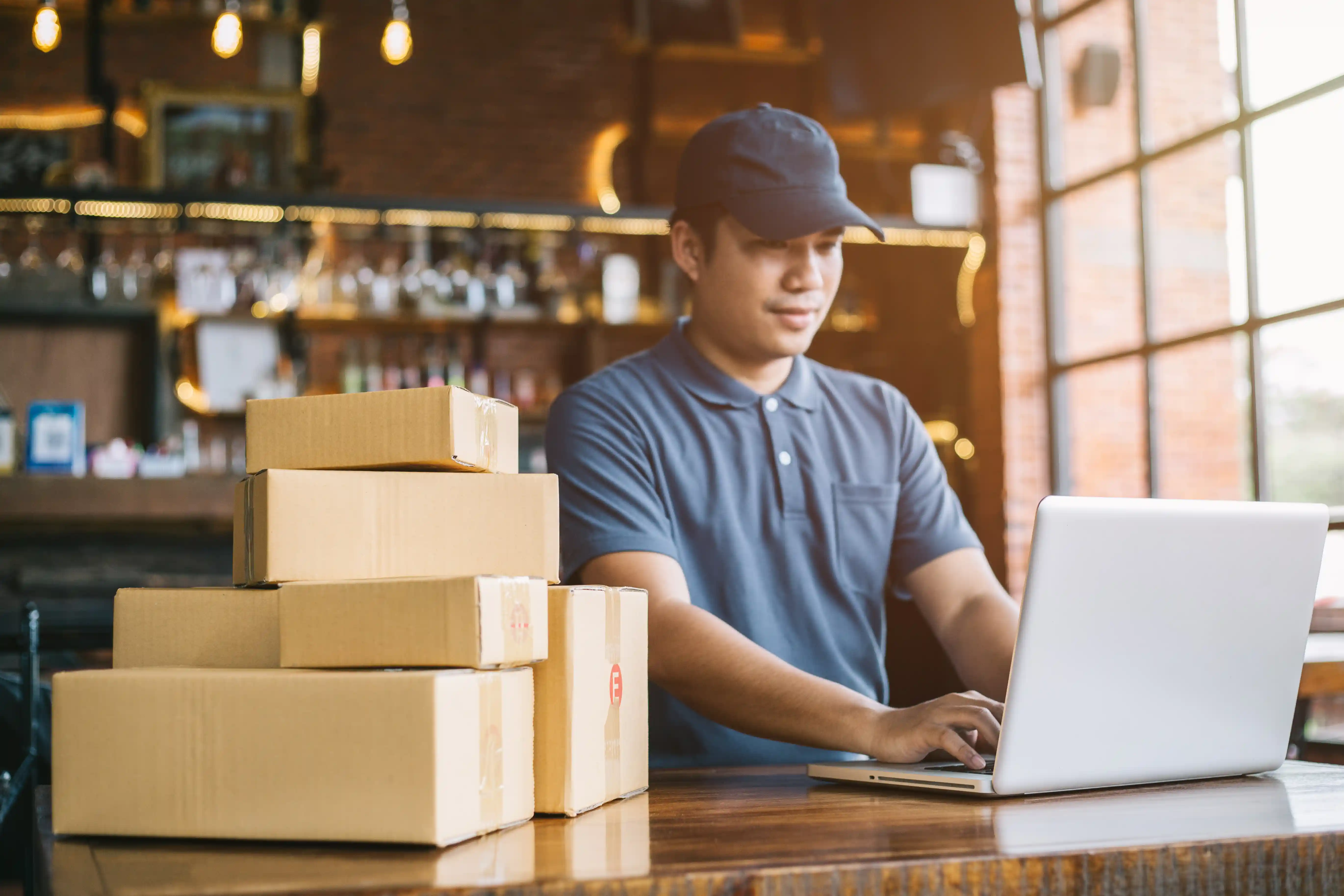 Man standing using laptop on desk with parcels stacked on top of desk