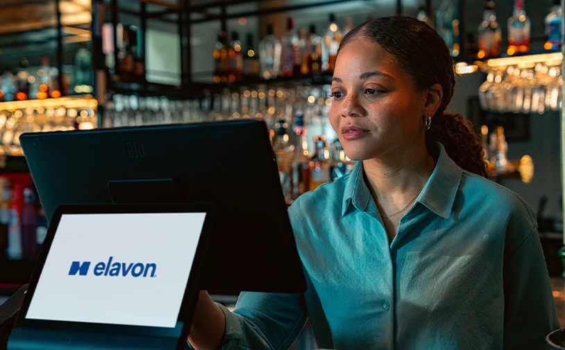 Hospitality staff member using an Elavon point of sale system to manage customer payments and business transactions at a bar