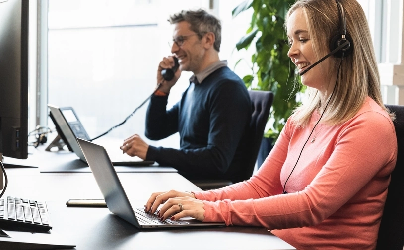 Two people working at a modern office desk with laptops and a phone, representing customer support operations in a professional setting