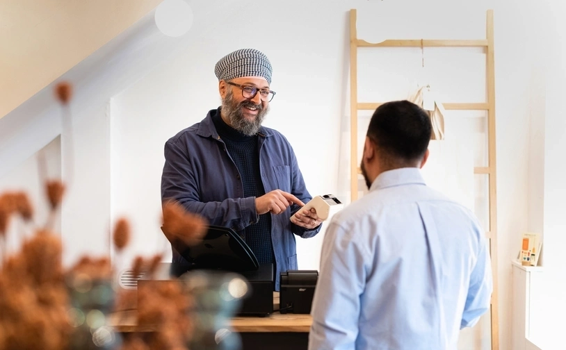  Shop assistant holding a portable card reader while processing a customer’s secure payment at the counter.